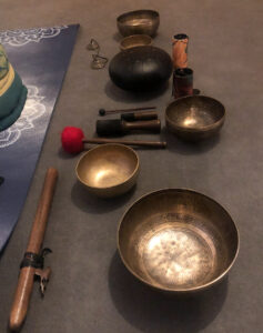 Plusieurs instruments de musique: Bols chantants, carillons et handpan exposés au sol à côté d'un tapis de yoga
