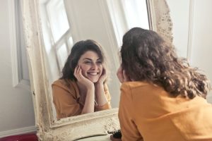 Une jeune femme se regarde dans un miroir en souriant, elle est heureuse, car elle a une bonne estime de soi